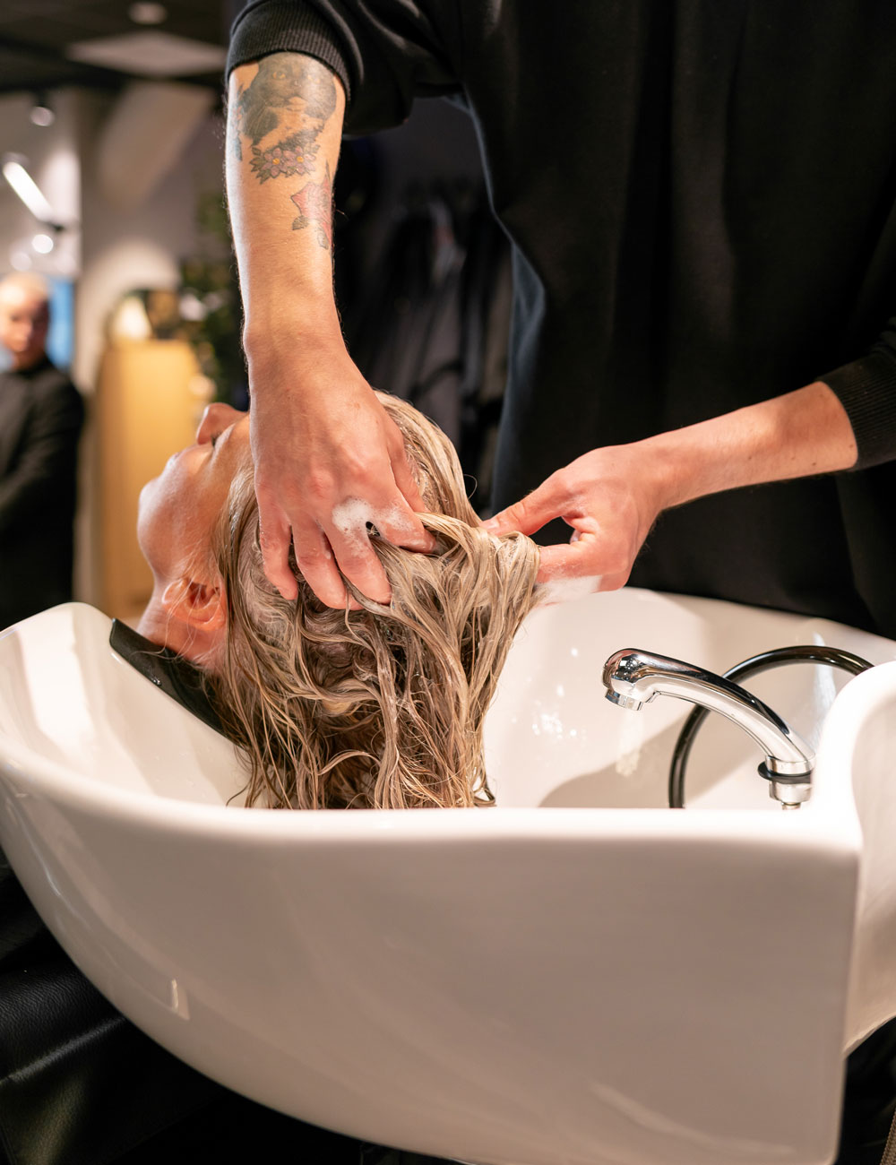 Smilende kunde i vaskestol hos Nikita Hair.