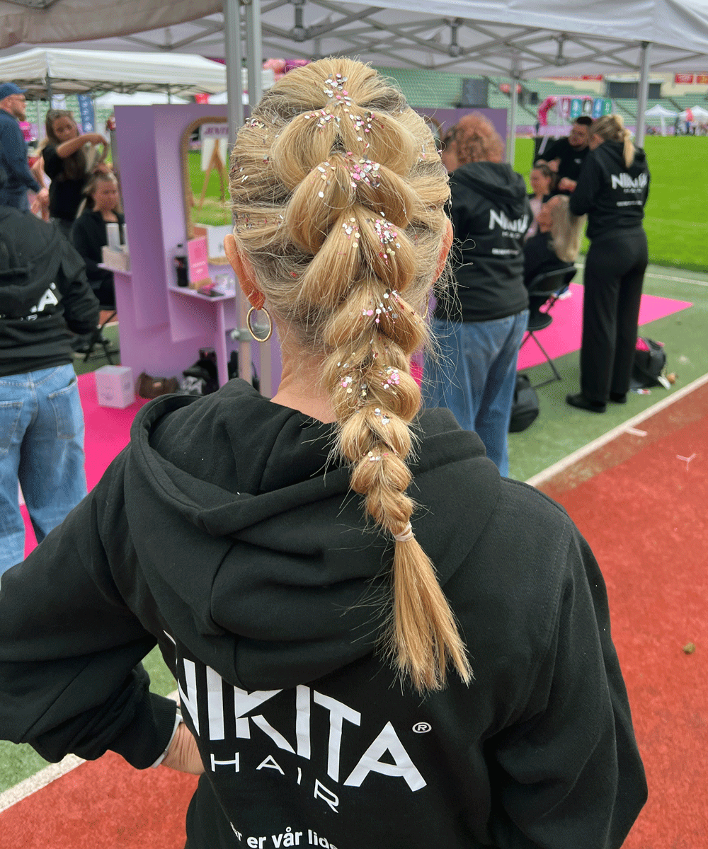 Frisør fra Nikita Hair styler deltaker med glitterflette under Jentemila 2025 i Oslo.