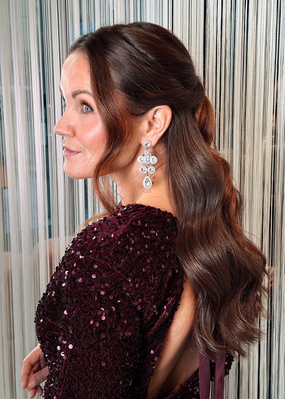 Halvt opp-frisyre med tvinnede partier og myke bølger i langt brunt hår, sett fra siden