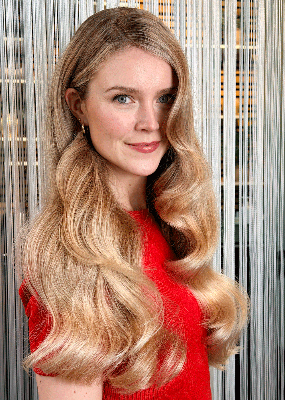 Langt blondt hår stylet i store, glansfulle Hollywood-bølger med dypt sideskille