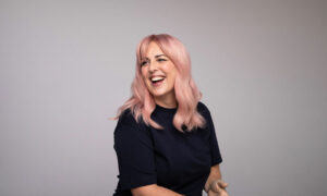 Person med pudderrosa hår i myke lengder, ferdig stylet mot nøytral bakgrunn