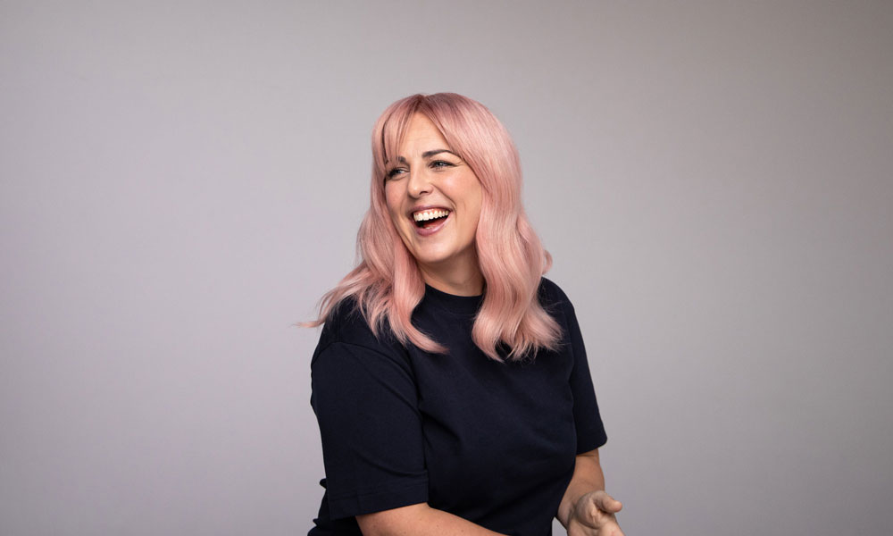 Person med pudderrosa hår i myke lengder, ferdig stylet mot nøytral bakgrunn