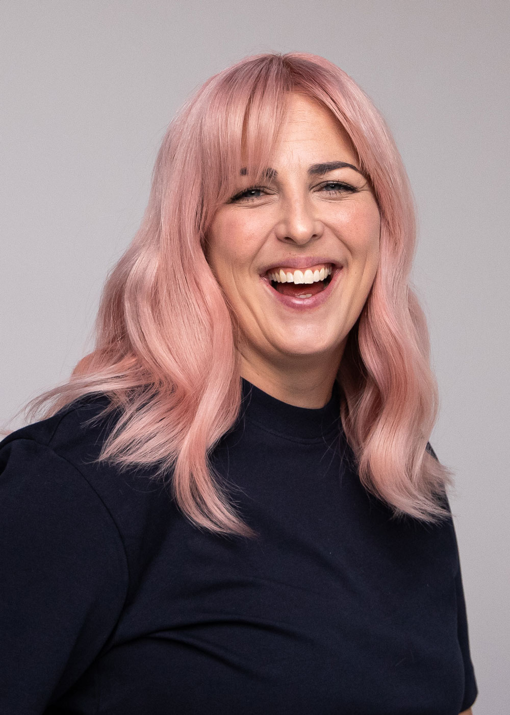 Nærbilde av person med pudderrosa hår i myke lengder, fotografert mot nøytral bakgrunn