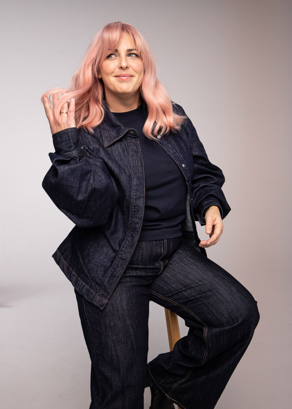 Person med pudderrosa hår og myke lengder, sittende og stylet i en avslappet, moderne look